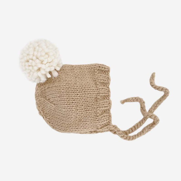Latte brown colored hand-knit winter bonnett. Features cream pom pom.
