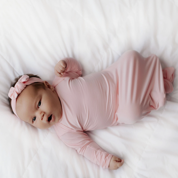 Light pink knotted baby gown with matching bow. This baby gown has super soft fabric, fold-over cuffs to prevent scratching, and the tie bottom makes middle of the night diaper changes so much easier.