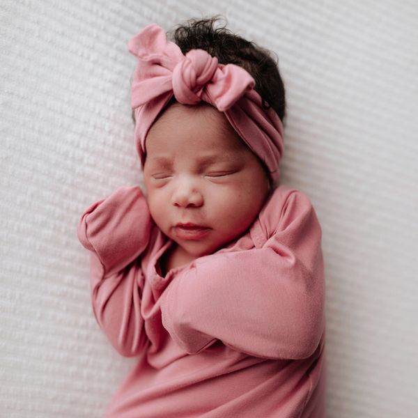 Knotted baby gown in rose color with matching bow. Features super soft fabric, fold-over cuffs, and tabs at shoulder for easy dressing.