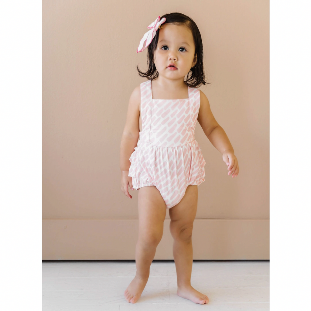 Girls bubble romper. White fabric with pink dash print. Features cross back straps, ruffles, and snaps for easy diaper changes. Sister match available! 
